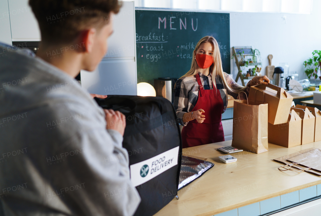 A waiterss handling orders in paper packages to courier for delivery. Concept of a take away food during pandemic.