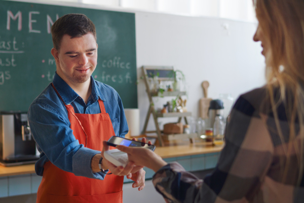 A cheerful young Down Syndrome waiter taking contactless smartphone payment from costumer in take away restaurant.