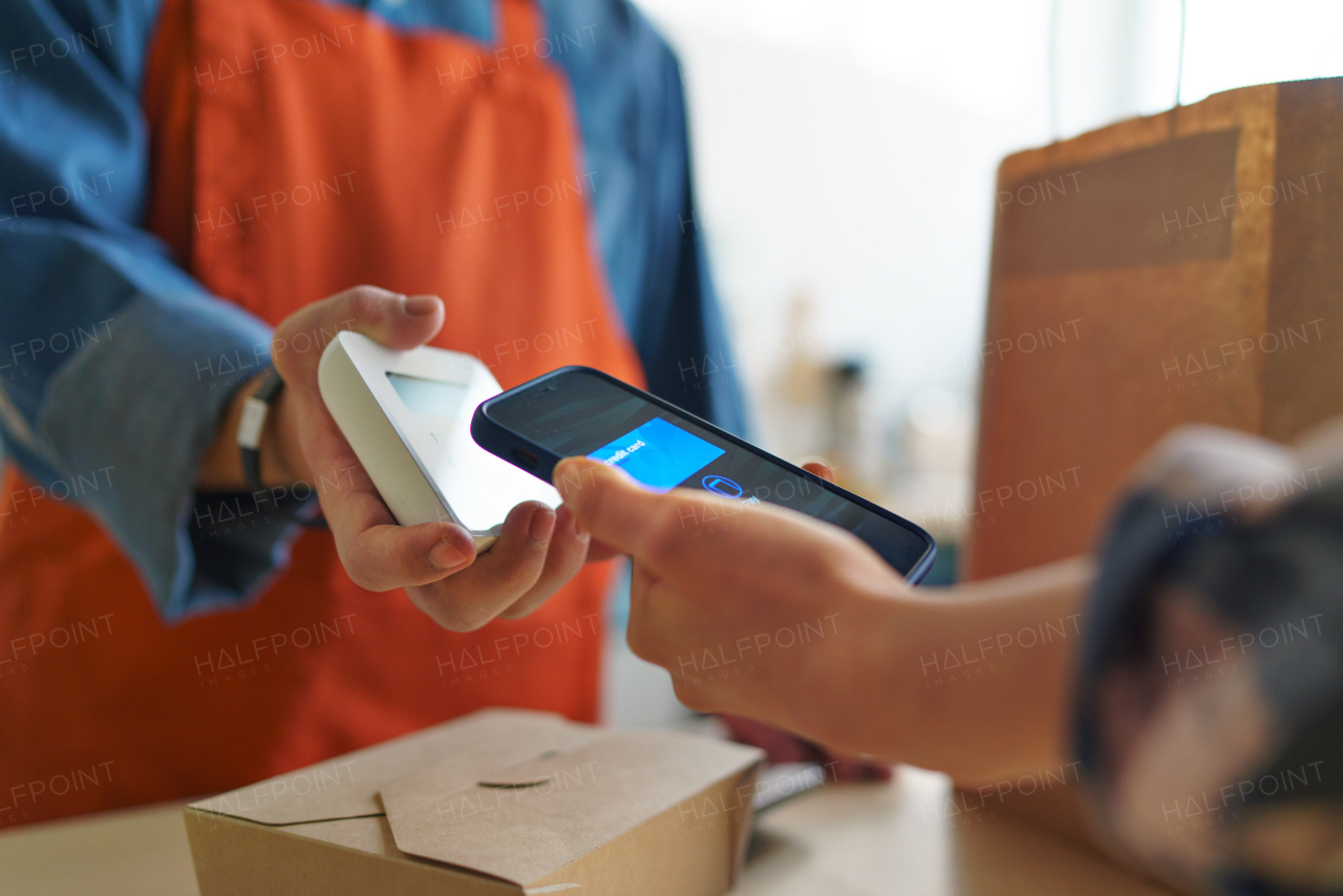 A close-up of waiter taking contactless smartphone payment from costumer in take away restaurant.