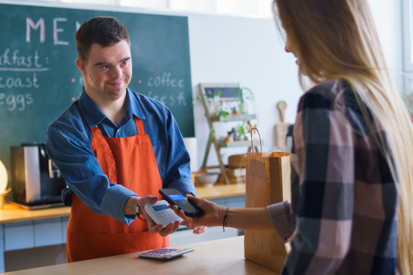 A cheerful young Down Syndrome waiter taking contactless smartphone payment from costumer in take away restaurant.