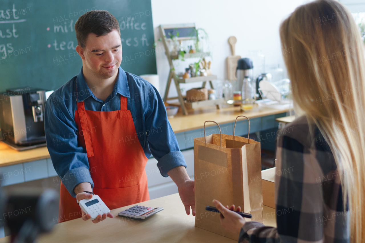 A cheerful young Down Syndrome waiter serving customer in take away restaurant, social inclusion concept.