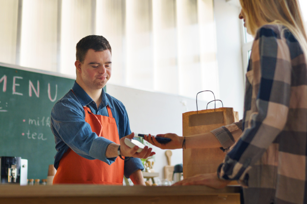 A cheerful young Down Syndrome waiter taking contactless smartphone payment from costumer in take away restaurant.