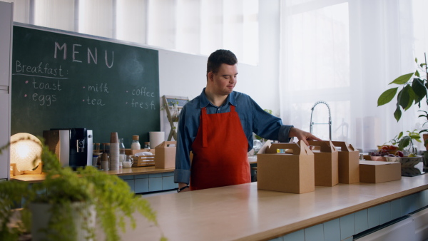 A cheerful young Down Syndrome waiter working in take away restaurant, social inclusion concept.