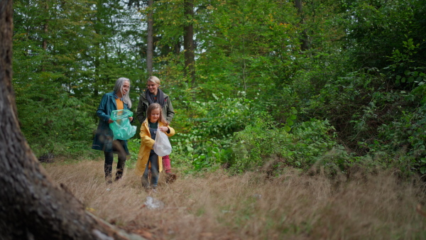 A small girl with mother and grandmother picking up waste outoors in forest.