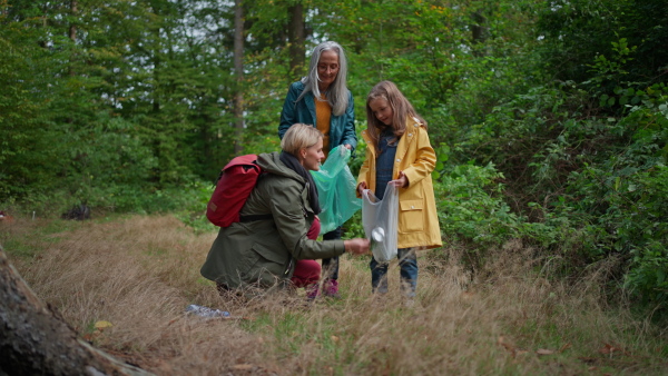 A small girl with mother and grandmother picking up waste outoors in forest.