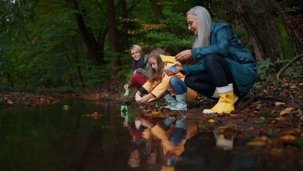 A small girl with grandmother picking up waste from little lake outoors in forest.