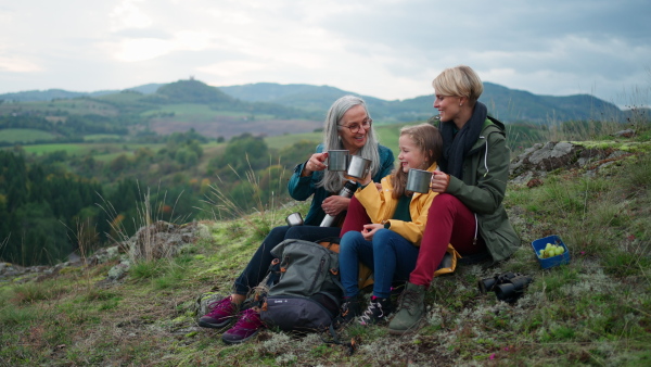 A small girl with mother and grandmother sitting and drinking hot tea on top of mountain.