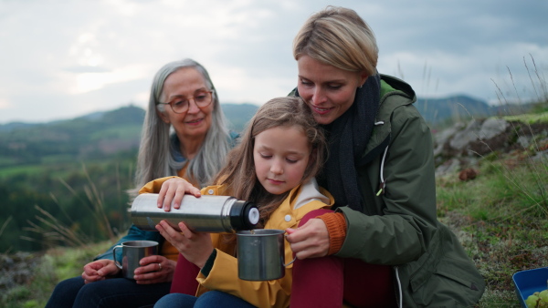 A small girl with mother and grandmother sitting and drinking hot tea on top of mountain.