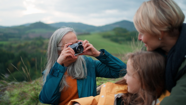 A senior woman taking picture of her daughter and granddaughter on top of mountain.