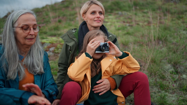 A small girl with mother and grandmother taking pictures with camera on top of mountain.