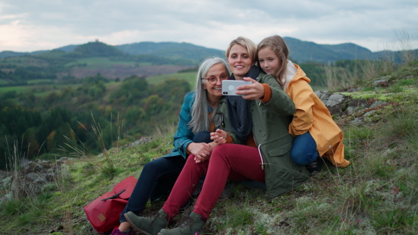 A small girl with mother and grandmother taking selfie outoors on top of mountain.