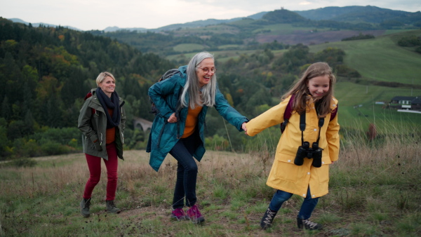 A portrait of small girl with mother and grandmother standing and looking at camera outoors in nature.