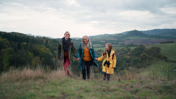 A portrait of small girl with mother and grandmother standing and looking at camera outoors in nature.