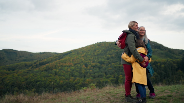 A small girl with mother and grandmother hikers hugging outoors in nature.