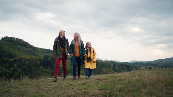 A small girl with mother and grandmother hodling hands and running outoors in nature.