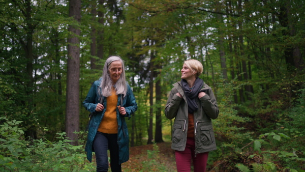 A senior mother with daughter on walk outoors in forest.