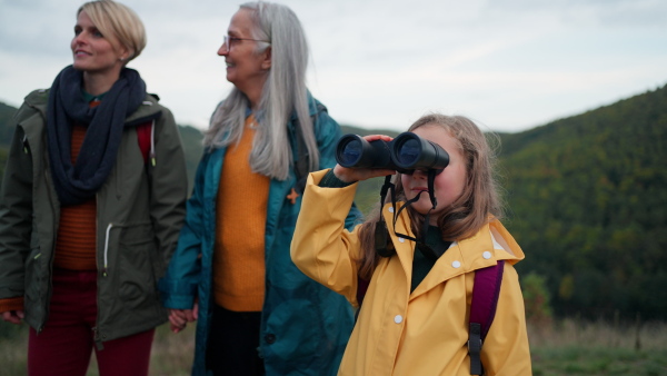 A small girl with mother and grandmother looking through binoculars on top of mountain.