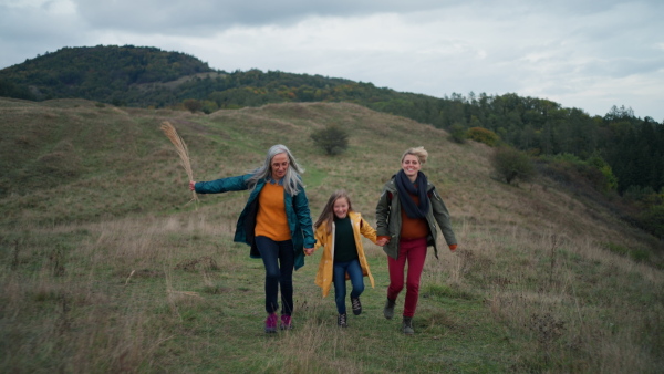 A small girl with mother and grandmother hodling hands and running outoors in nature.