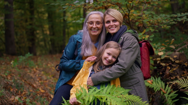 A small girl with mother and grandmother on walk outoors in forest, looking at camera.