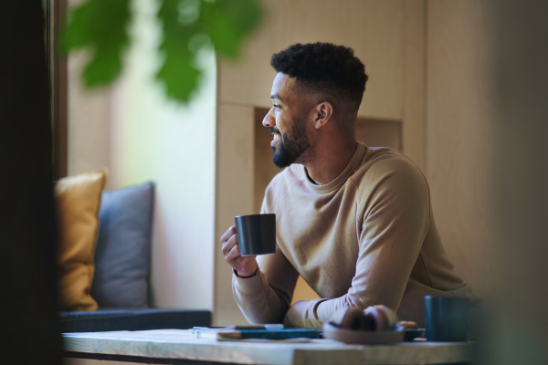 A happy young man with coffee sitting indoors in a tree house, weekend away and individual traveling concept.