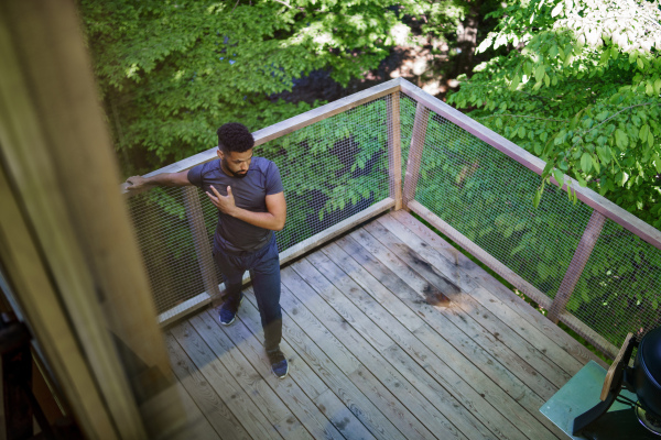 A high angle view of happy young man doing exercise outdoors on terrace of tree house, weekend away and digital detox concept.