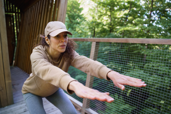 A happy mid adult woman doing exercise outdoors on terrace of tree house, weekend away and digital detox concept.