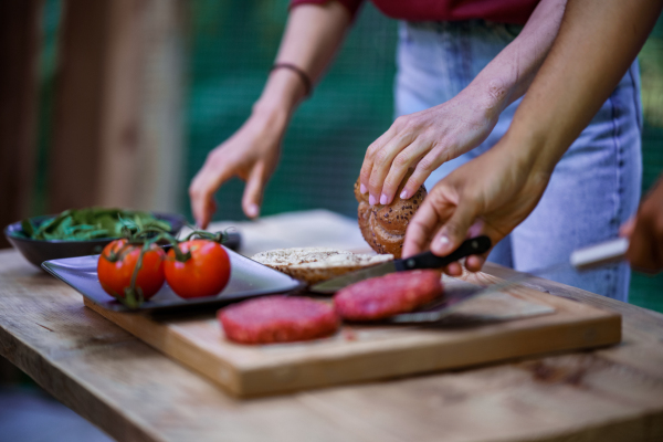 A raw minced hamburger meat prepared for grilling. Homemade grilled hamburgers. Close-up of hands preparing dinner outdoors on the patio.