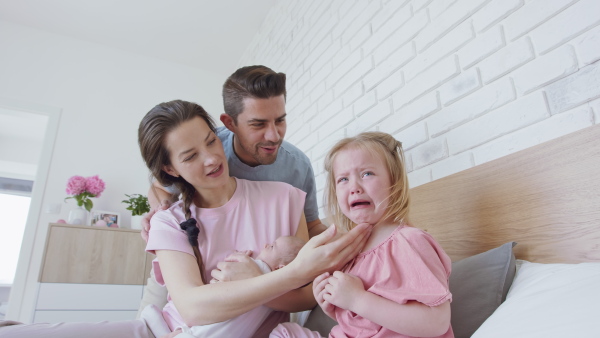 A happy young family with newborn baby calming down little daughter crying indoors at home.