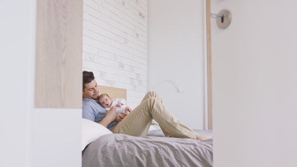 A young father enjoying time together with newborn baby girl, lying on bed at home.