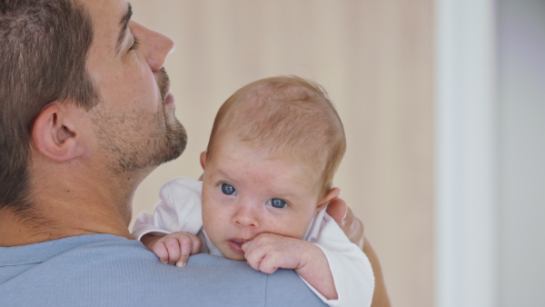 A close up of young father holding his newborn baby girl at home.