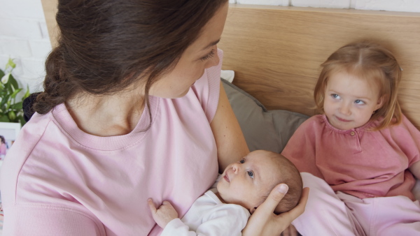 A happy young mother with newborn baby and little girl enjoying time together at home.