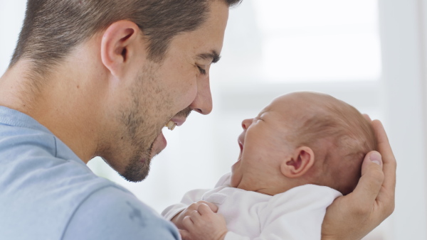 A close up of young father enjoying time together with crying newborn baby girl at home.