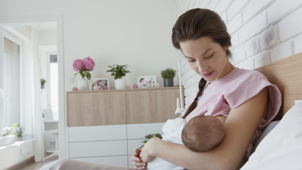 A young mother breastfeeding her newborn baby girl indoors at home, maternity leave.