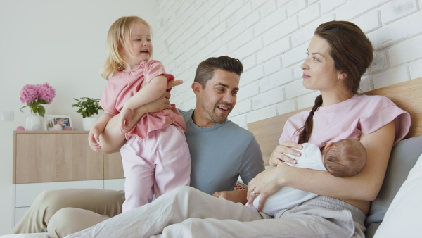 A happy young family with newborn baby and little girl enjoying time together at home.