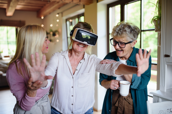 Happy senior women friends having fun with Virtual Reality Glasses imndoors at home.