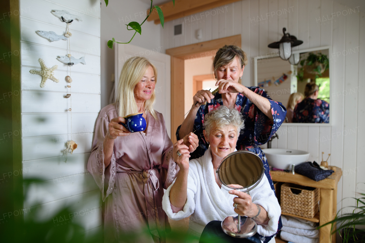 Happy senior women friends in bathrobes having fun indoors in a bathroom, selfcare concept.