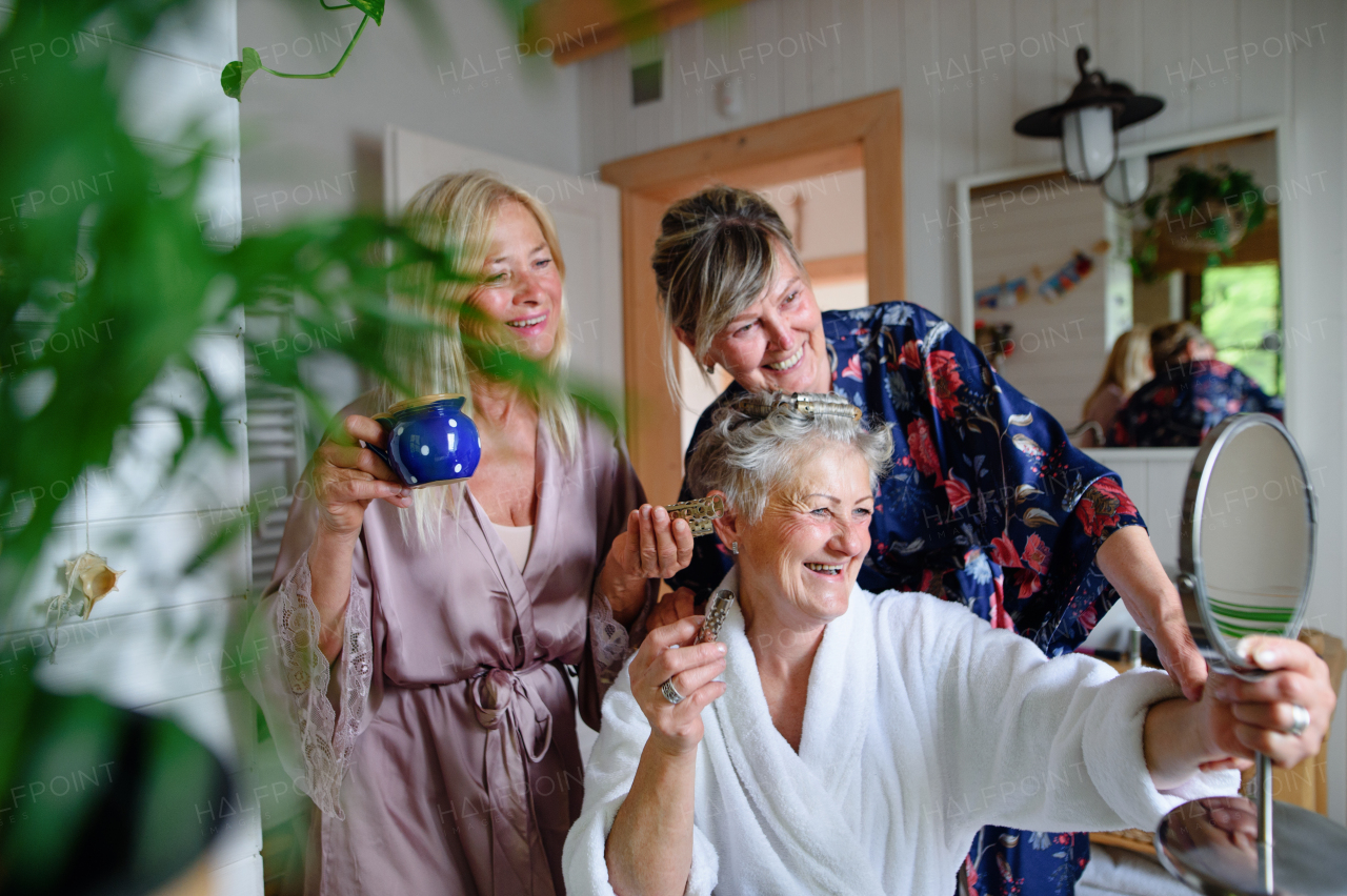 Happy senior women friends in bathrobes having fun indoors in a bathroom, selfcare concept.