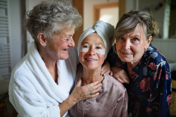 Happy senior women friends in bathrobes looking at a camera indoors at home, selfcare concept.