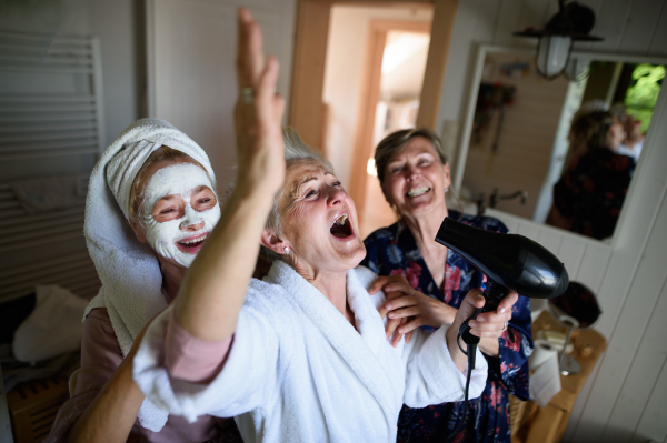 Happy senior women friends in bathrobes having fun indoors at home, a selfcare concept.