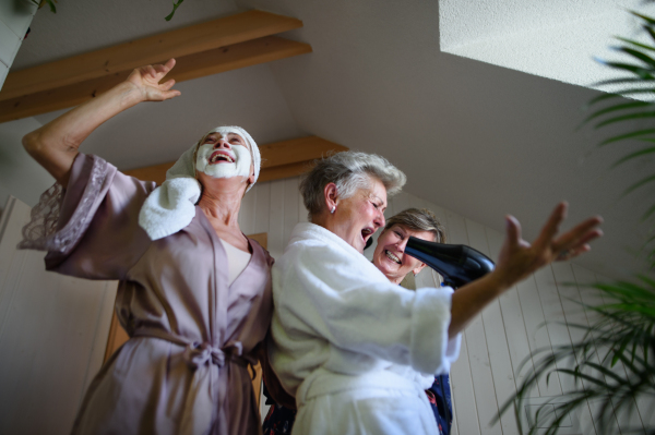 A low angle view of happy senior women friends in bathrobes having fun indoors at home.