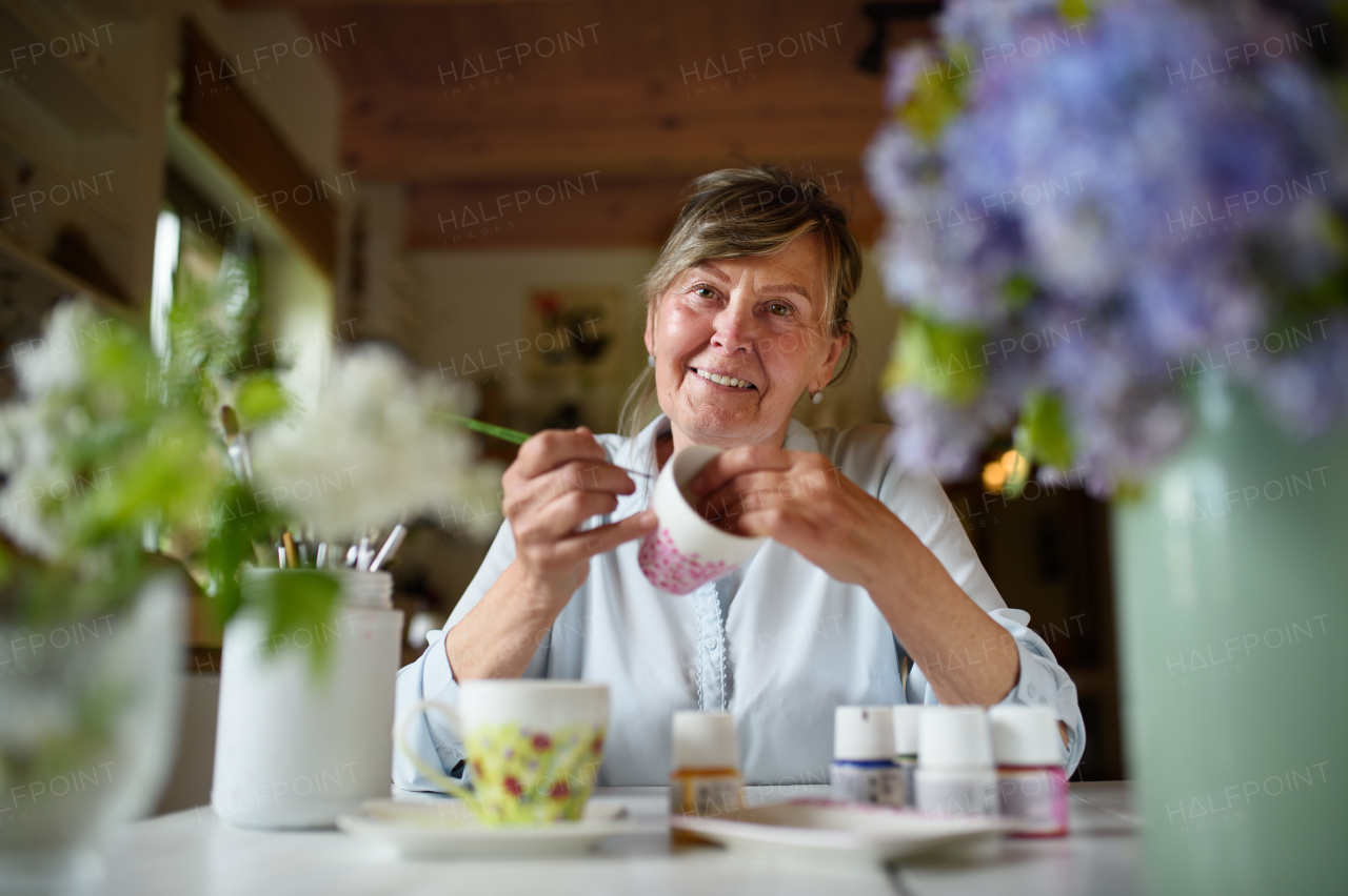 Low angle view of a happy senior artist woman painting cermaic cup, artcraft concept.