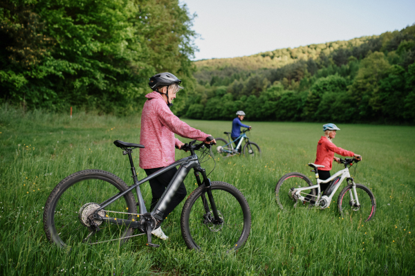 Happy active senior women friends cycling together outdoors in nature in meadow.