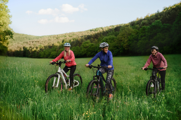 Happy active senior women friends cycling together outdoors in nature in meadow.