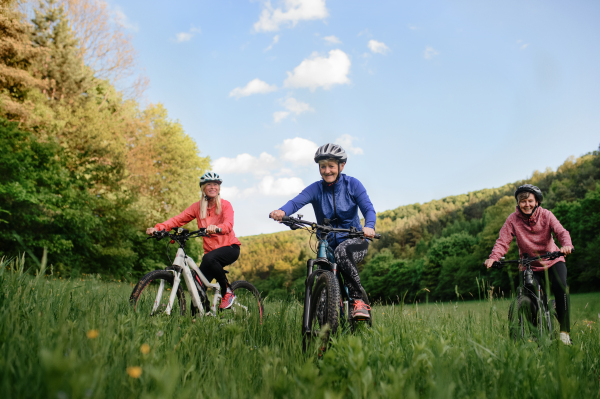 Happy active senior women friends cycling together outdoors in nature in meadow.