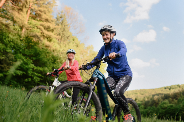 Happy active senior women friends cycling together outdoors in nature in meadow.