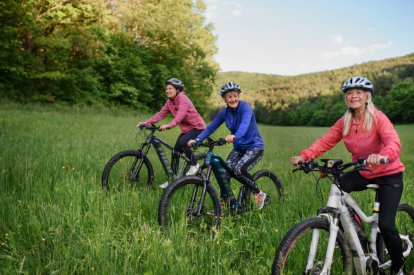 Happy active senior women friends cycling together outdoors in the nature.