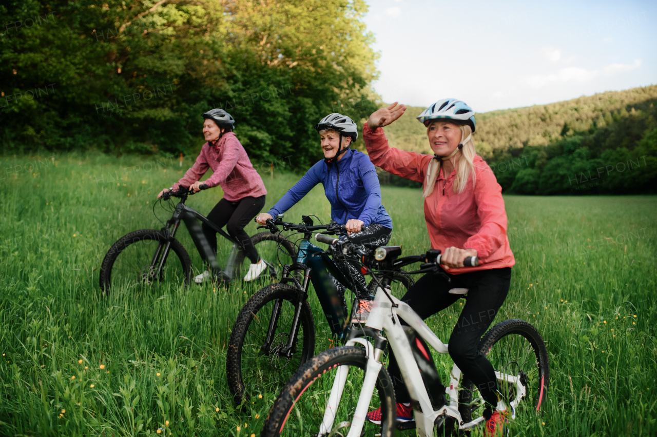 Happy active senior women friends cycling together outdoors in nature in meadow.