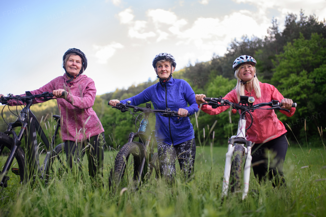 Happy active senior women friends cycling together outdoors in nature in meadow.