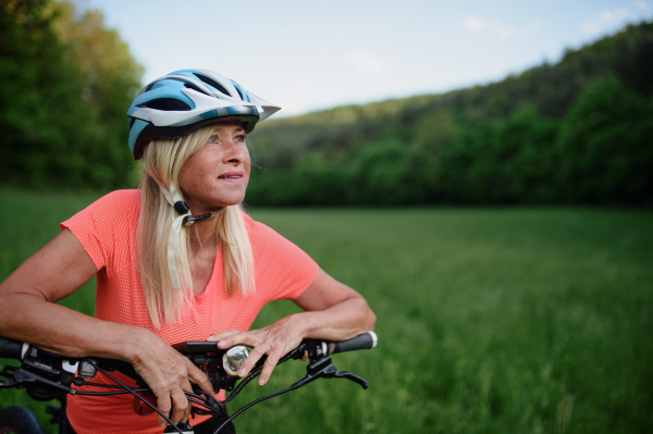 A cheerful active senior woman biker outdoors in nature.