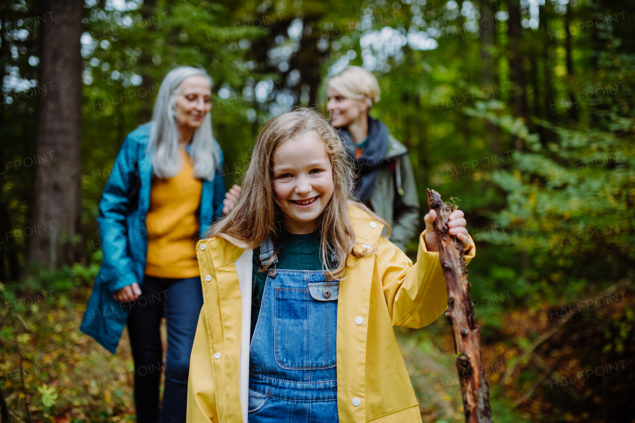 A happy little girl with basket running during walk with mother and grandmother outdoors in forest